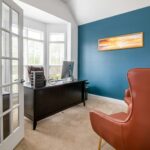 Bright office room with blue accent wall, featuring leather chair and desk in natural light.